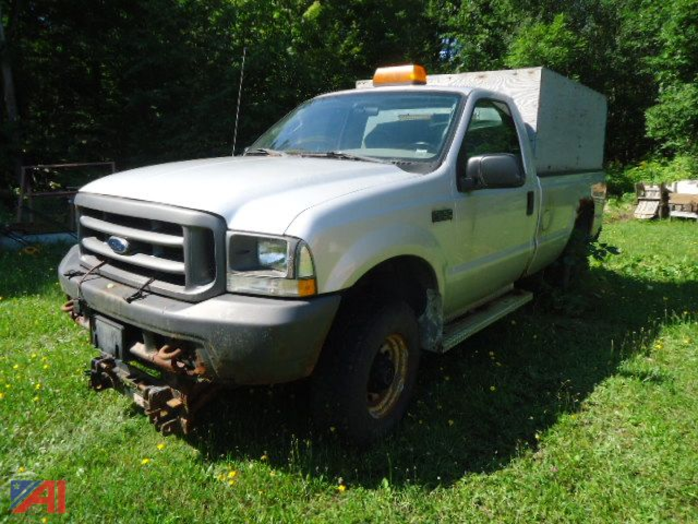 Ford F-250 Super Duty pickup truck with plow mount and utility box in grassy lot, front view showing bumper and headlight.