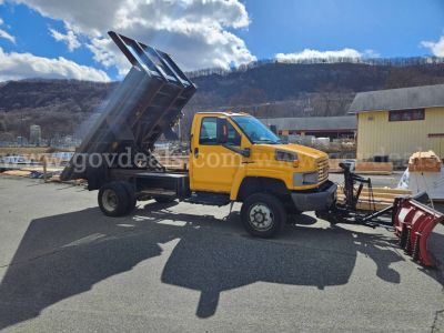 GMC C4500 dump truck with yellow cab and raised bed, flatbed dump in operating angle.
