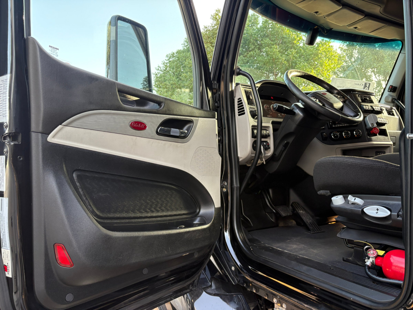 Peterbilt 579 truck interior door and driver cockpit view showing steering wheel, dashboard, and open door with inner panel.