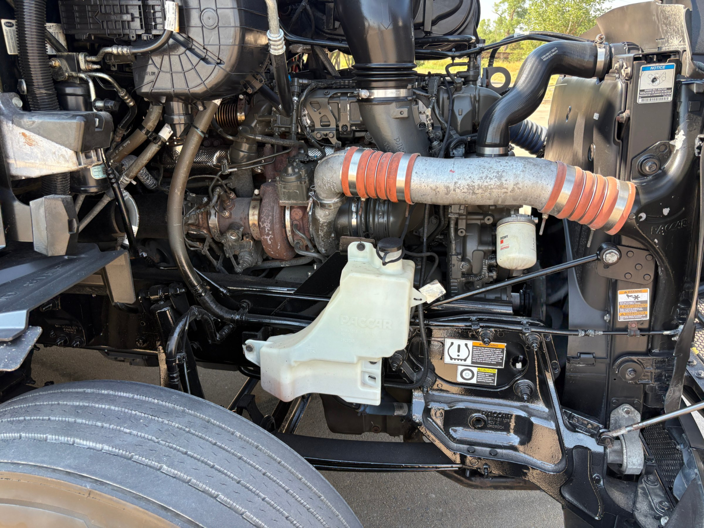 Peterbilt 579 engine bay with visible fuel lines, coolant reservoir, intercooler piping, and turbocharger connections.