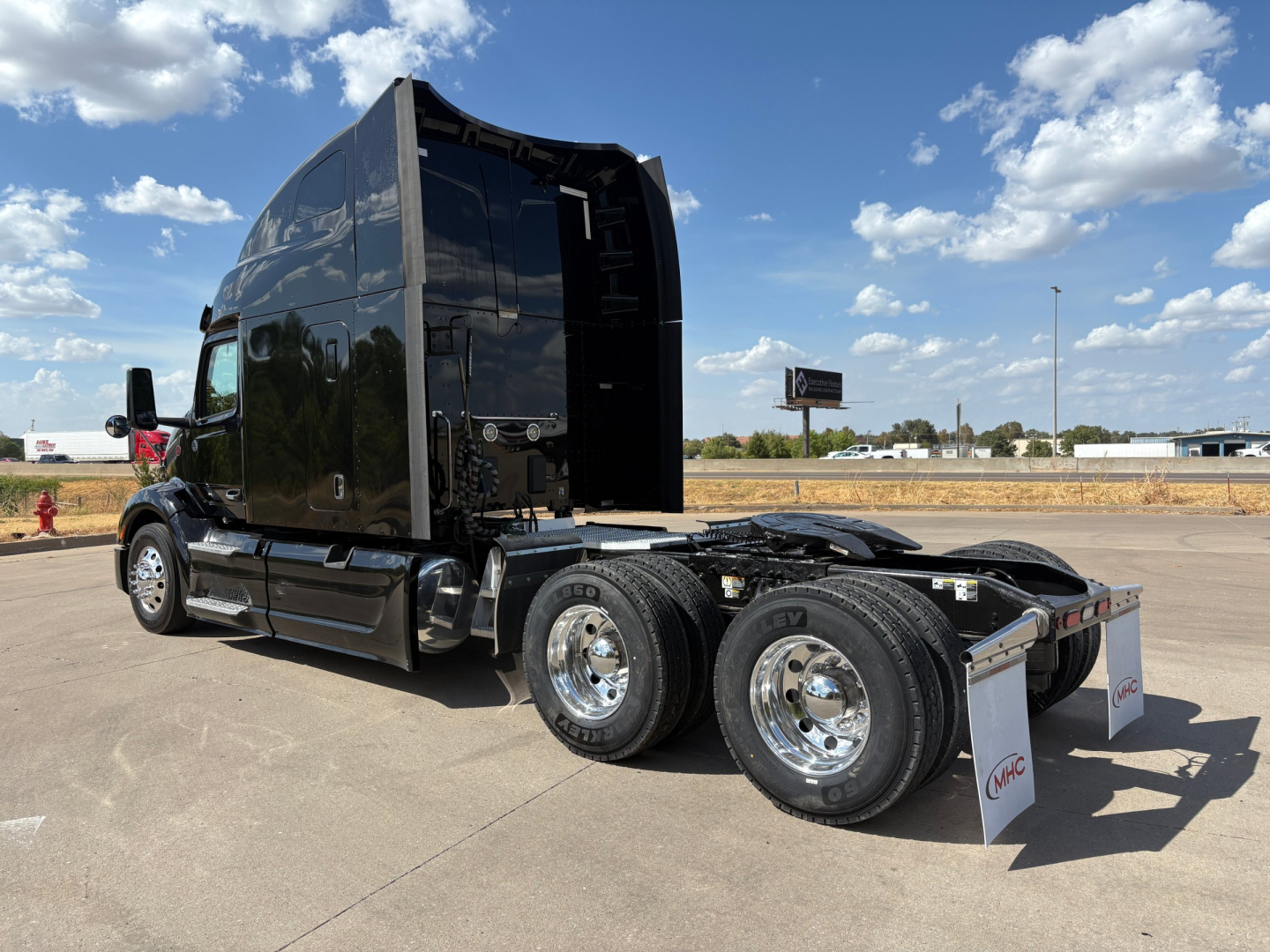 Peterbilt 579 tractor in a parking lot, black sleeper cab, dual rear axles, chrome wheels. Visible text on image not readable due to distance.