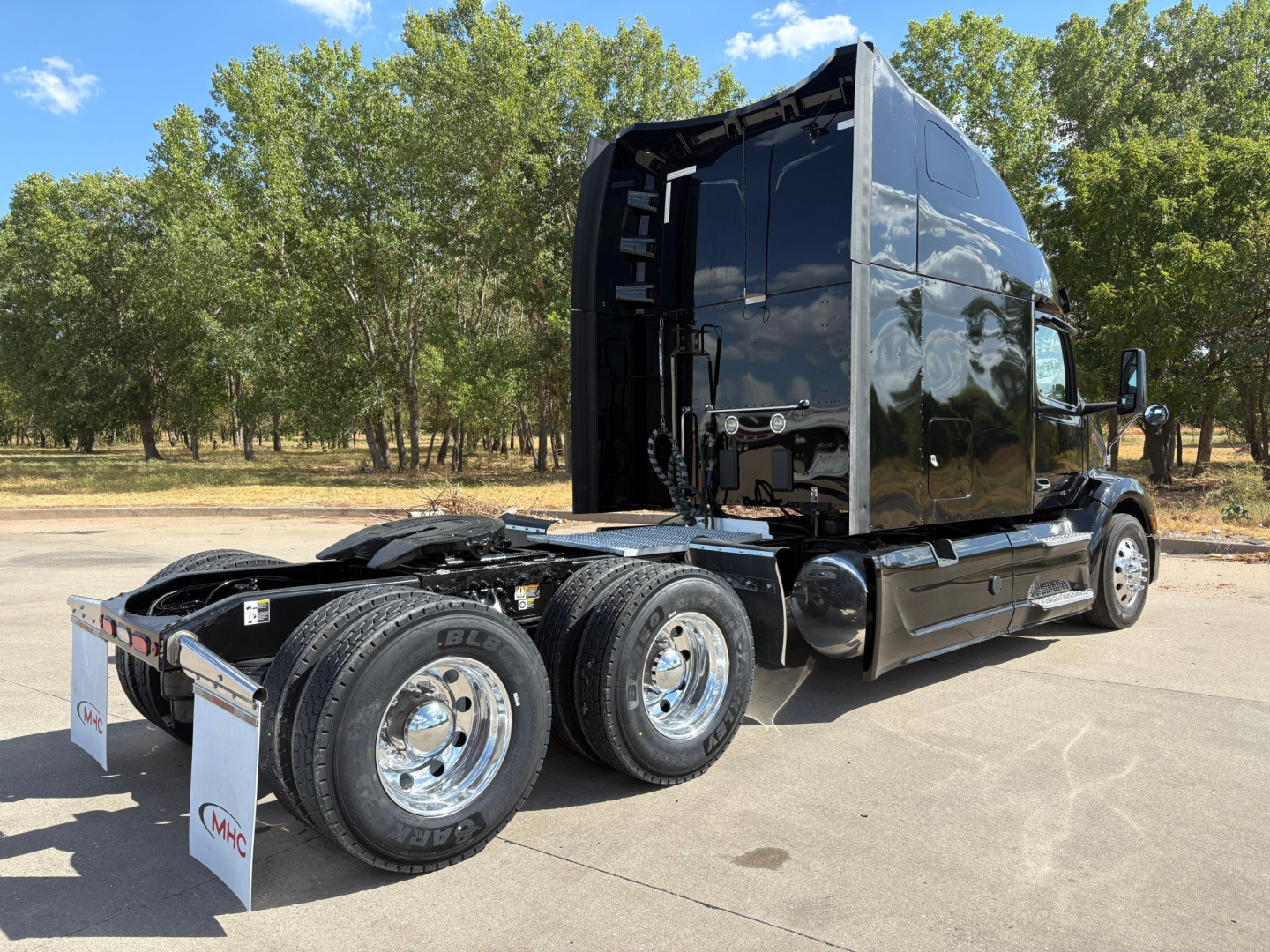 Peterbilt 579 truck cab and dual rear axles in a parking lot, glossy black exterior, chrome wheels, Fifth wheel area visible, side mirrors, tall sleeper cab