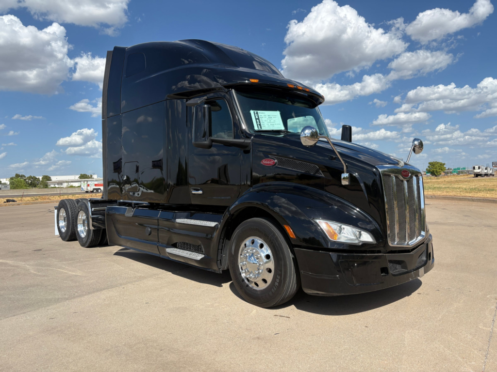 Peterbilt 579 conventional sleeper truck in black, side view showing aerodynamic hood, chrome wheels, cab mirrors, and triple rear axles.