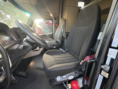 Truck cab interior of a 2022 Peterbilt 579 showing driver's seat with adjustment controls, steering wheel, dashboard, and open door with labels.