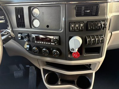 Peterbilt 579 dash area with control switches, gauges, and key in ignition. Visible text includes DPF? not clear; multiple circular gauges, row of toggle switches, climate controls, cup holders. No clear legible model text.