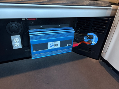 In-cab area of a Peterbilt 579 showing a blue portable inverter/charge device mounted under the dash with a circular cigarette lighter style outlet and a blue ringed plug connected to a power receptacle.