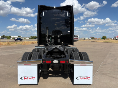 Peterbilt 579 tractor rear view showing fifth wheel, dual rear axles, and white MHC mud flaps with red MHC logo.