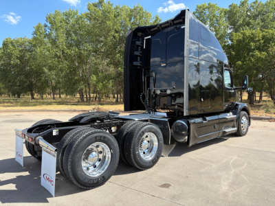 Peterbilt 579 truck cab and dual rear axles in a parking lot, glossy black exterior, chrome wheels, Fifth wheel area visible, side mirrors, tall sleeper cab