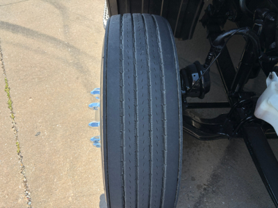 Conventional sleeper Peterbilt 579 wheel/tire and part of suspension visible with tire tread, blue fasteners on wheel studs.