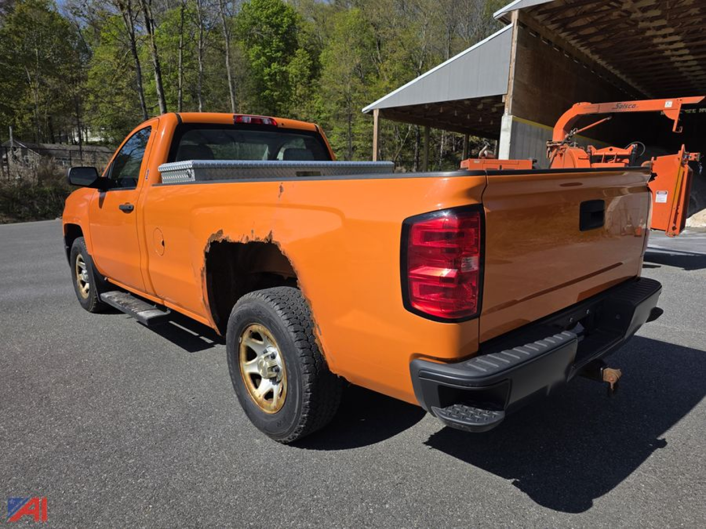 Rear and left side view of a bright orange 2015 Chevrolet Silverado 1500 pickup in a lot, showing bed, rear bumper, taillight, and wheel; pickup appears used.