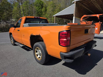 Rear and left side view of a bright orange 2015 Chevrolet Silverado 1500 pickup in a lot, showing bed, rear bumper, taillight, and wheel; pickup appears used.