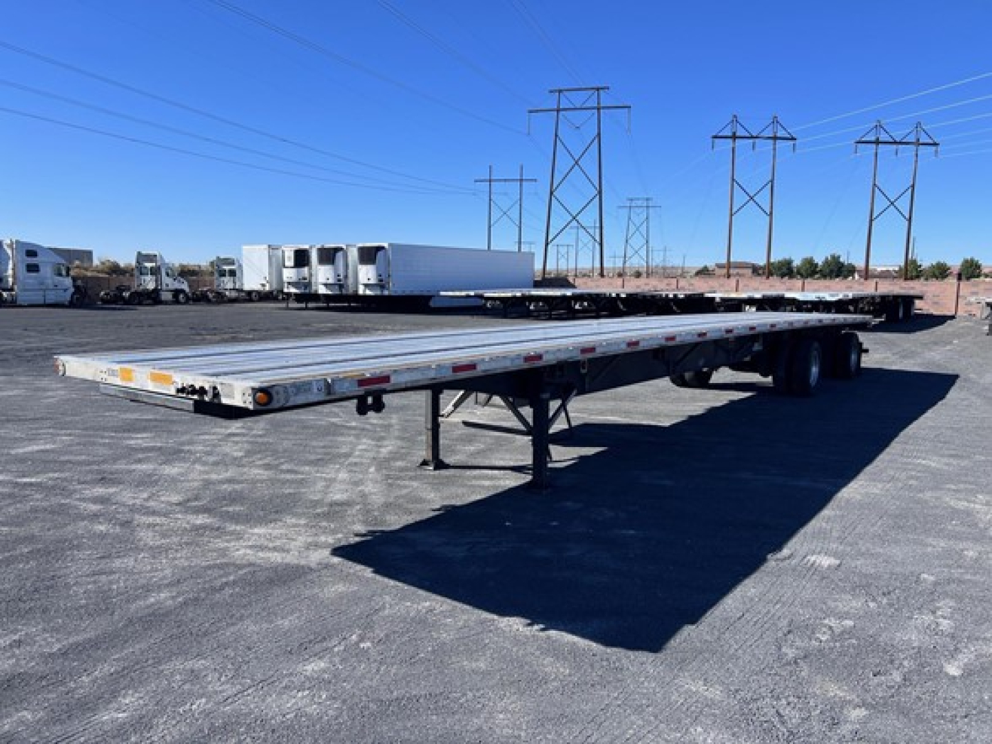 Long flatbed trailer in a parking lot showing a 2024 Utility 4000Ae with low deck and tandem axles. Serial numbers and details not legible.