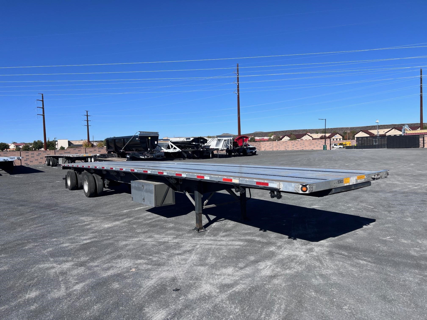 Flatbed trailer showing Utility 4000AE in a gravel lot with clear blue sky and distant buildings.