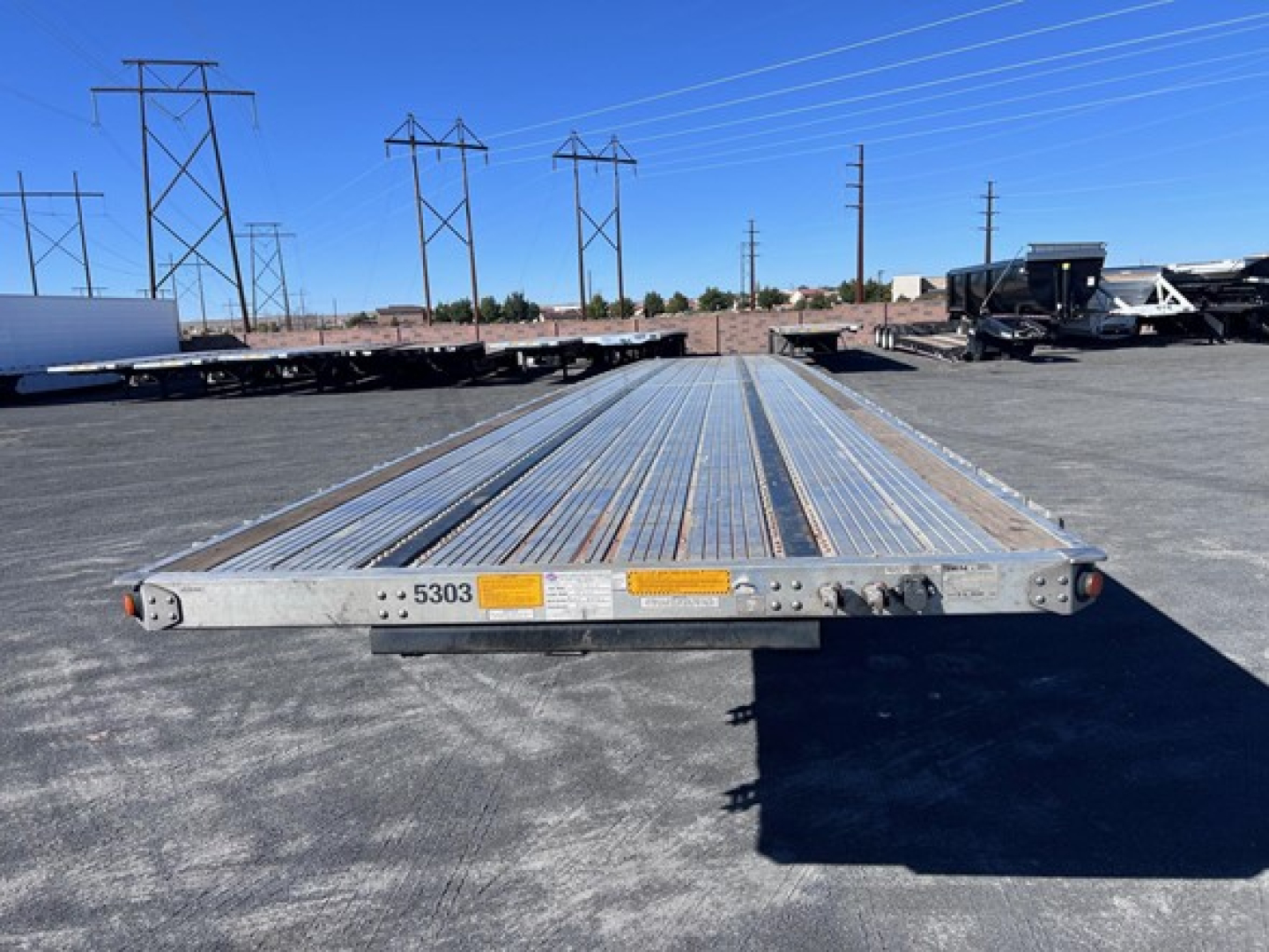 Flatbed trailer deck showing long aluminum planks with end plate and small labels on the front edge.