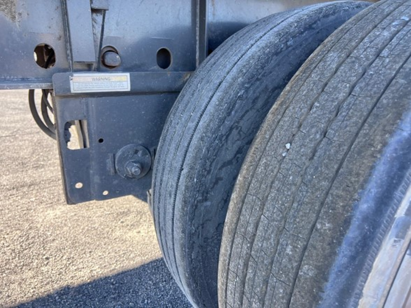 Trailer dual wheel close-up showing metal frame and wheels of a Utility 4000Ae flatbed trailer, part of chassis with warning label