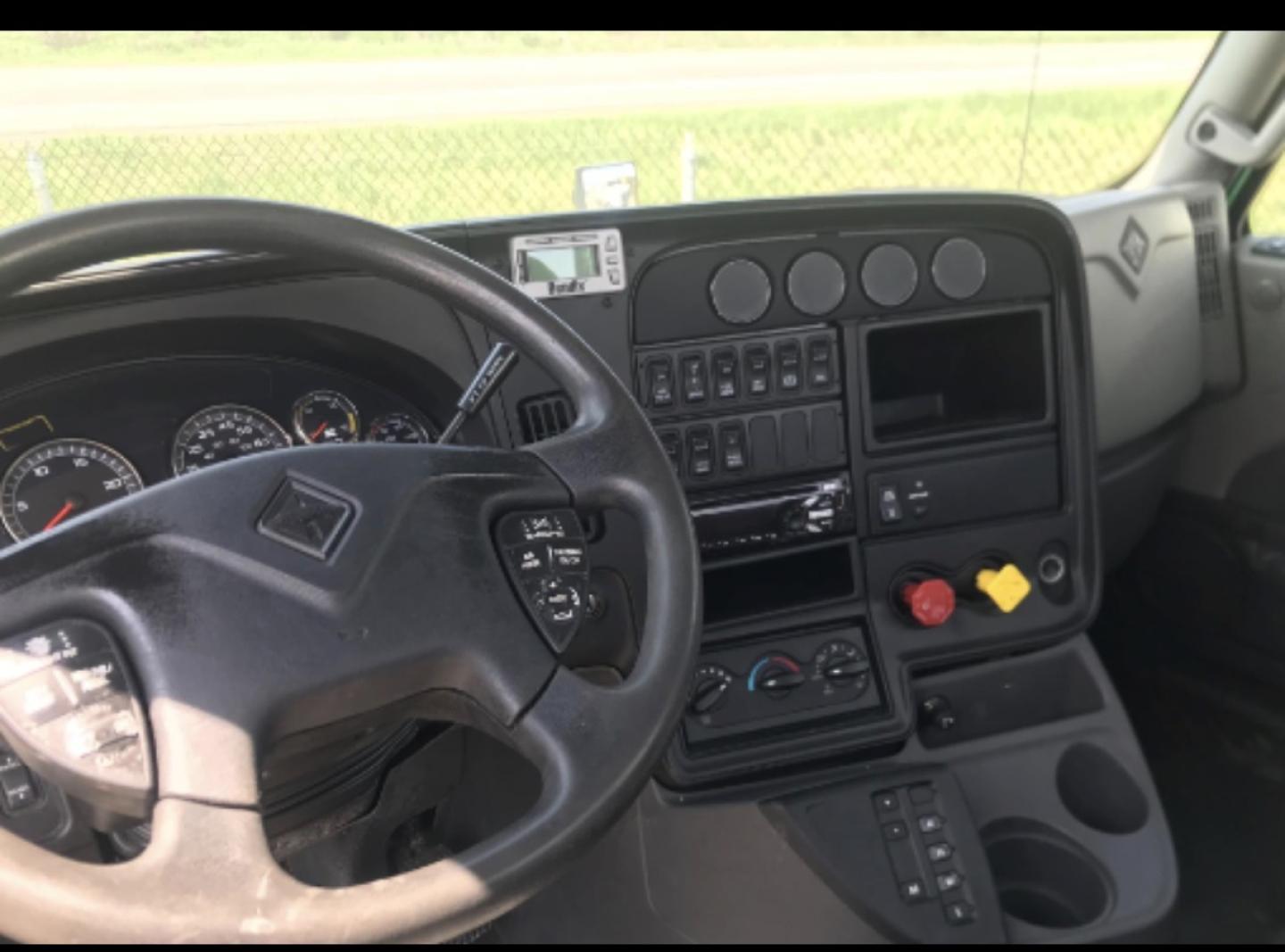 Truck cab interior showing steering wheel, dashboard, gauges, and center console with switches and cupholders.