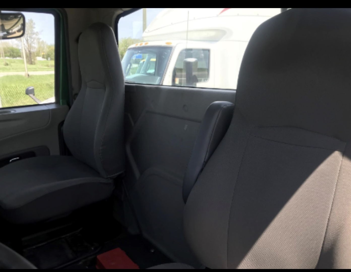 Truck cab interior showing front driver seat and rear bench seat with gray fabric upholstery; window and exterior truck visible through glass.