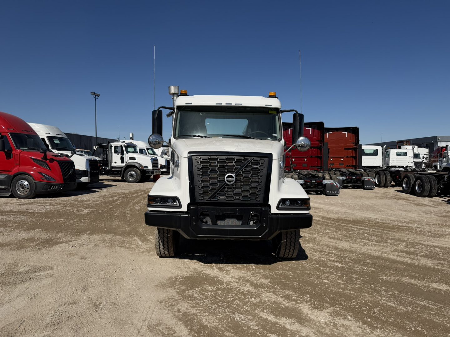 Front view of a white Volvo VHD86B300 truck in a dealership lot, grille badge visible, with other trucks in background.