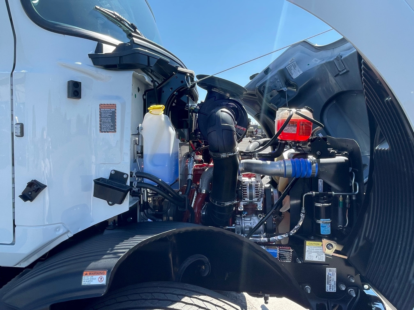 Truck engine bay of a 2025 Mack MD6 showing front left side with coolant reservoir and various hoses and components.