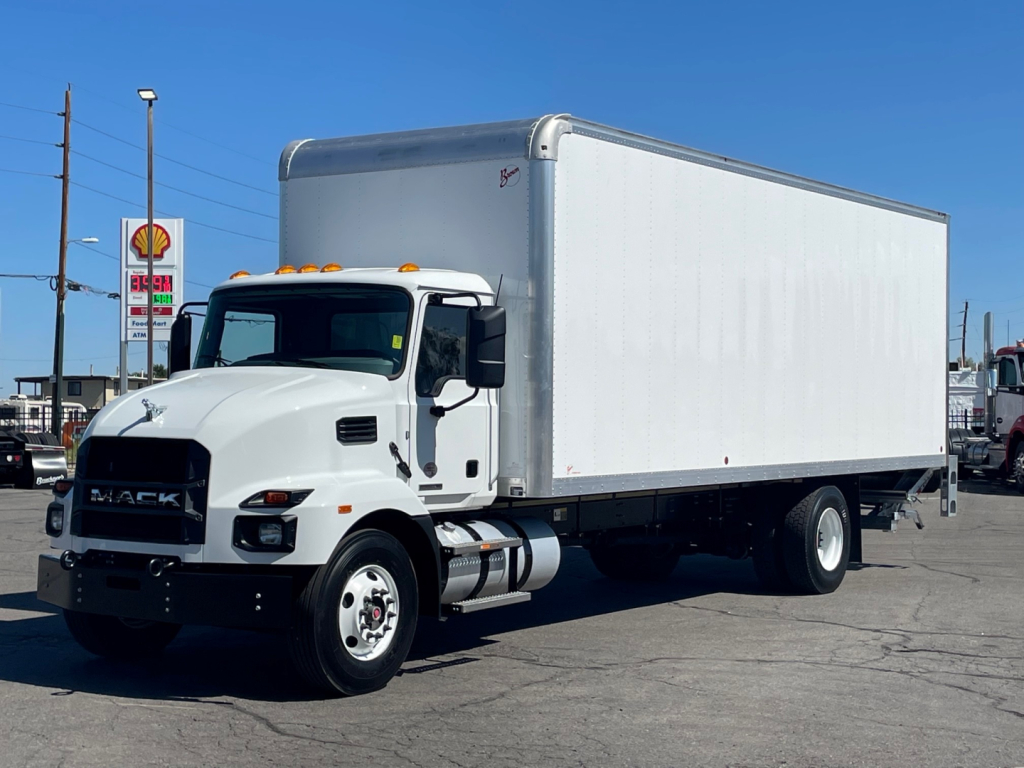 Box truck in a dealership lot showing a white 2025 Mack MD6 box truck with a large cargo box and dual rear wheels.