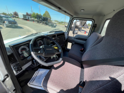 Truck cab interior showing steering wheel and dashboard of a 2025 Mack MD6 with gray seats and large windshield.