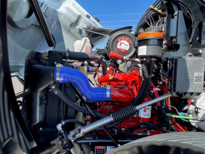 Mack MD6 engine bay showing blue intercooler pipe, red engine block, and various hoses and gauges.