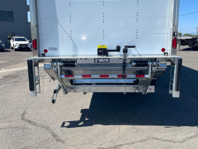 Rear view of a white Mack MD6 box truck showing liftgate with WALTEC label and dual vertical stabilizers.