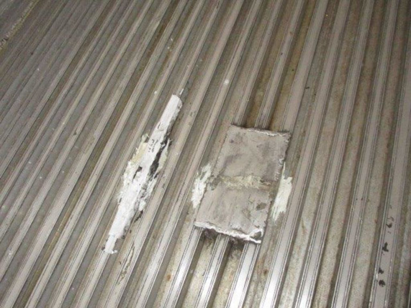 Trailer interior showing corrugated metal floor with a rectangular patched area and white residue.