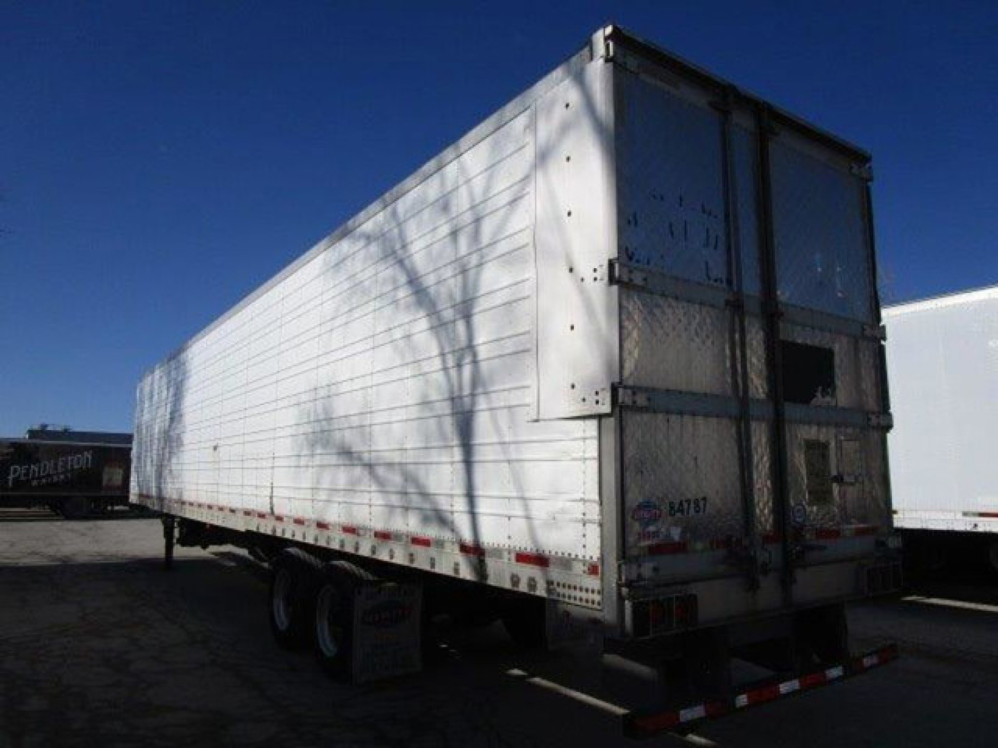 Reefer trailer side and rear with white aluminum panels; tandem axles; rear doors visible; undercarriage and reflectors show.