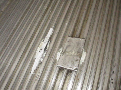 Trailer interior showing corrugated metal floor with a rectangular patched area and white residue.