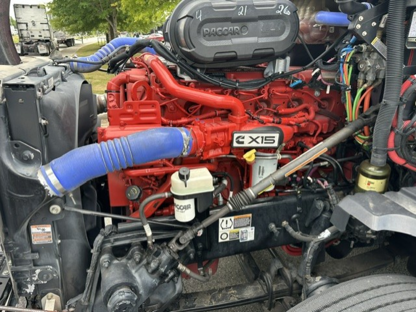 Red Cummins engine with bright blue hoses and CX15 badge in Kenworth T680 engine bay showing coolant hose and various labels.