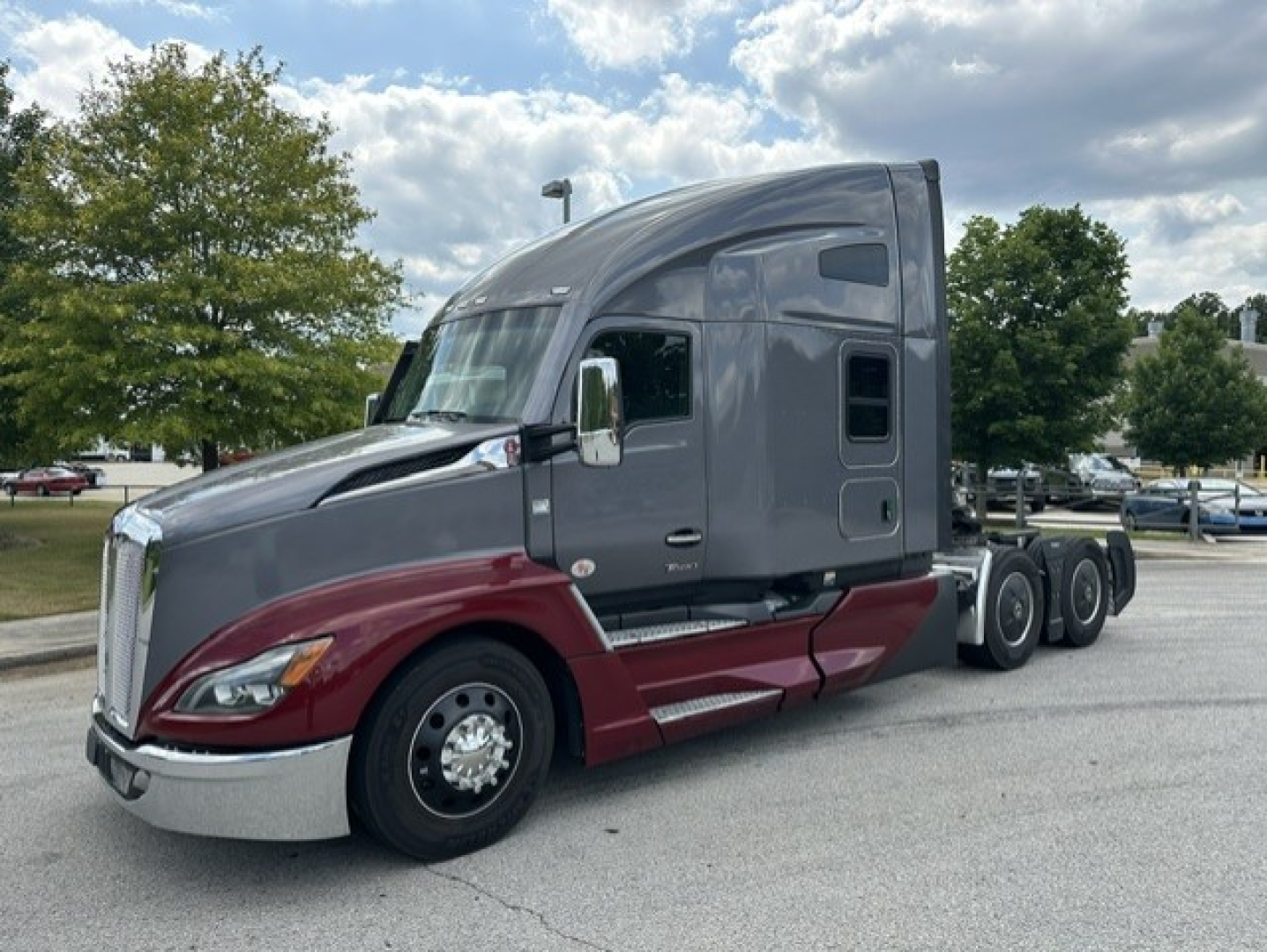 Kenworth T680 conventional sleeper truck in two-tone gray and maroon shown from front-left; dual rear axles; chrome bumper and wheels; windshield, side windows, and aerodynamic cab details visible.