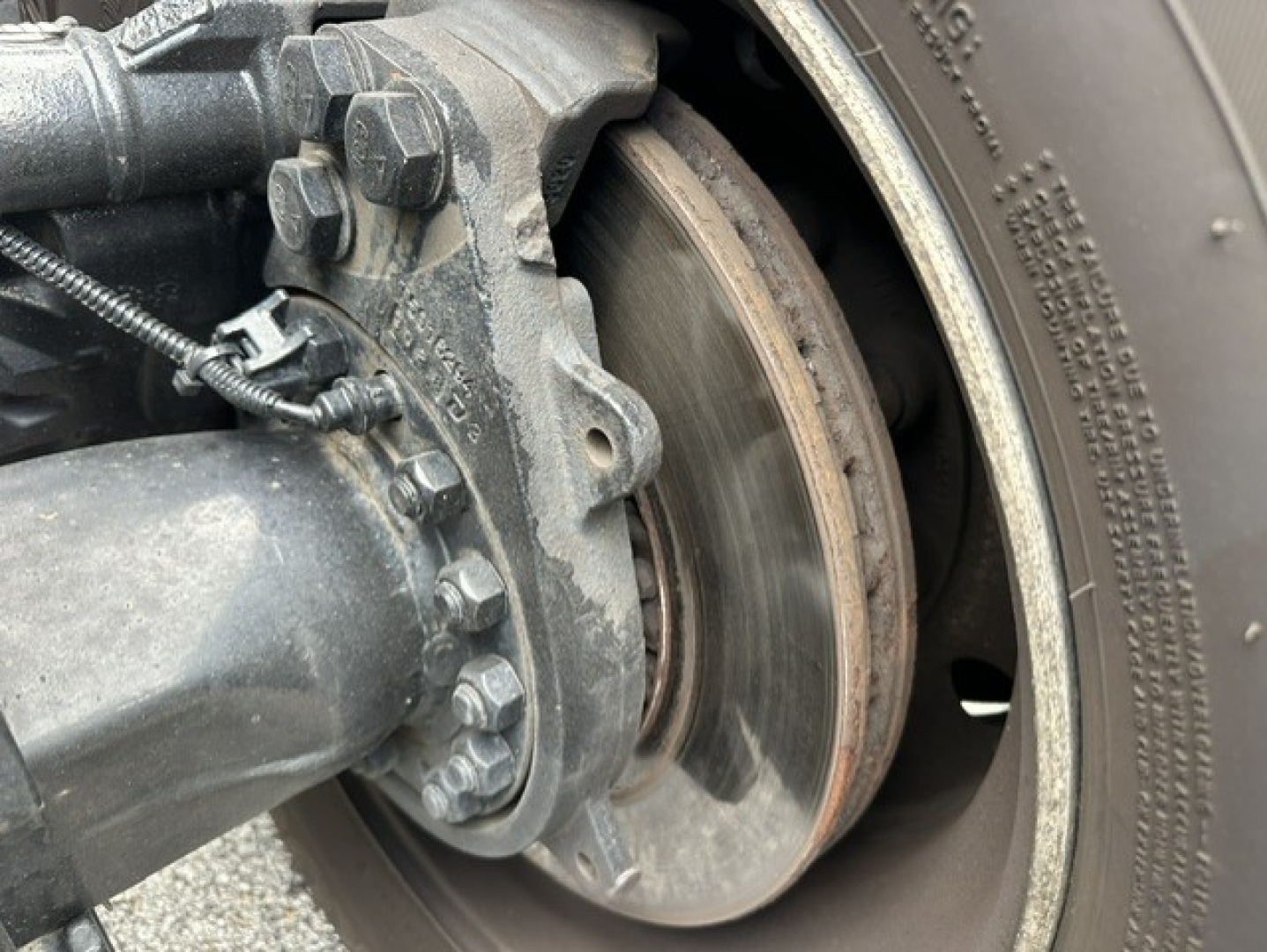 Kenworth T680 wheel and brake assembly showing rotor, caliper mounting bolts, hub, and tire sidewall.