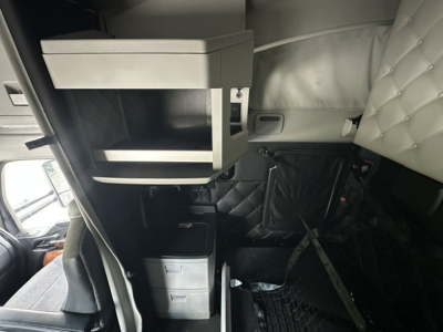 Kenworth T680 cabin interior showing storage box and control modules with quilted light-gray upholstery and driver area.