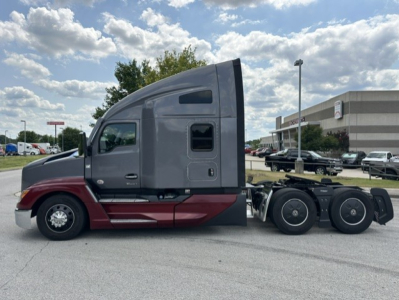 Kenworth T680 conventional sleeper truck side view showing gray cab with maroon lower accent and triple rear axles.