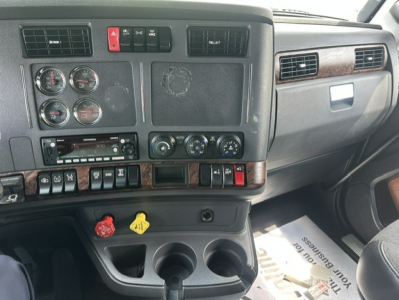 Dashboard and center console of a Kenworth T680 truck cab showing instrument gauges, controls, climate knobs, cup holders, and cup holders area.