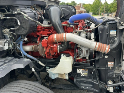 Kenworth T680 engine bay showing red engine block with blue hose, black intake tubes, and various metal and plastic components.