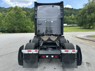 Kenworth T680 rear view showing fifth wheel, dual rear axles, and mud flaps; rear chassis with hoses and electrical connections, gray cabin undercarriage, highway background.