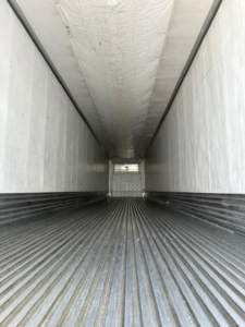 Trailer interior with ribbed flooring and high walls; rear opening visible, white insulated ceiling inner lining along sides.