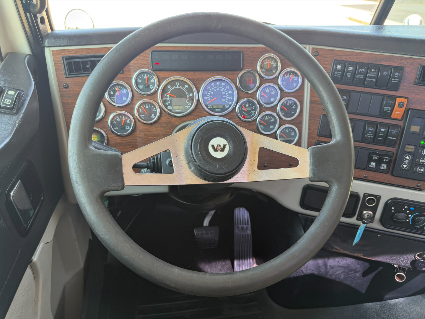 Truck cab dashboard with multiple gauges and wooden panel; steering wheel centered with Western Star logo; various switches and gauges visible.