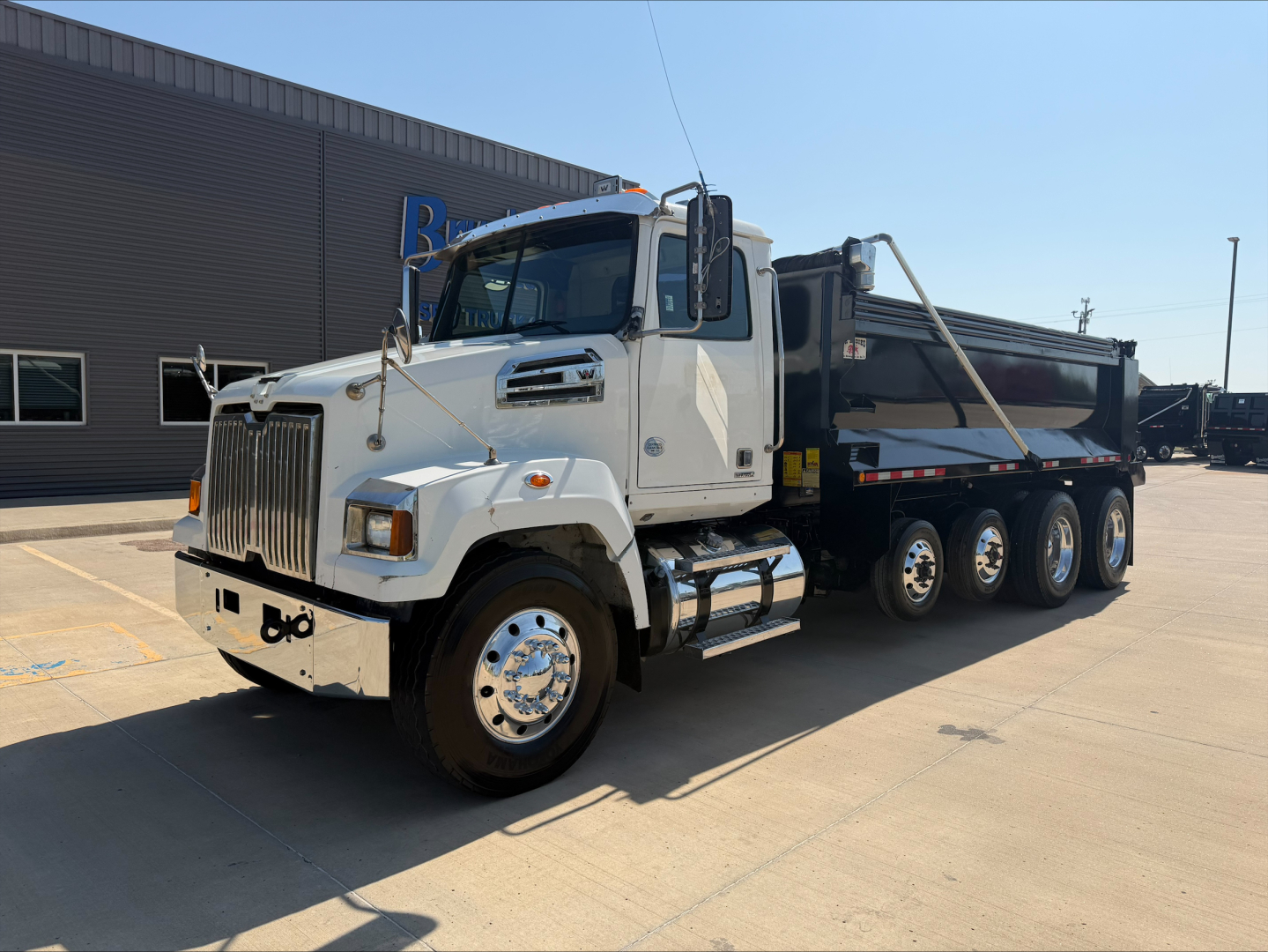Western Star 4700SF dump truck side view showing front grille, cab, and dump bed with triple rear axles.