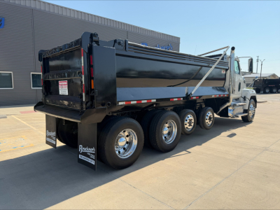 Dump truck side view showing a black dump body with multiple axles and chrome wheels. Visible text on rear mud flaps reads 'Brad's' and license plate area blank. Cabin area and hydraulic components not legible.