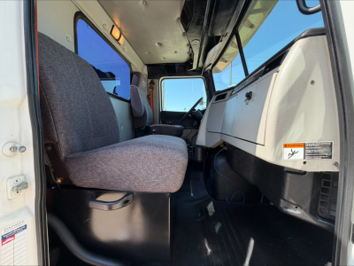 Interior of a Western Star 4700SF cab showing driver seat, passenger seat, dashboard, and door with warning label.