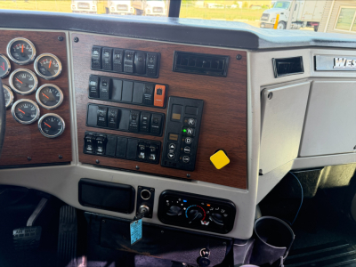 Interior of a 2017 Western Star 4700SF dash showing analog gauges, wooden trim, and control panels with switches.