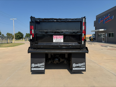 Back view of a used 2017 Western Star 4700SF dump truck with black dump bed, warning label on tailgate, and Bruckner’s Oklahoma City mudflaps; dealership building in background.