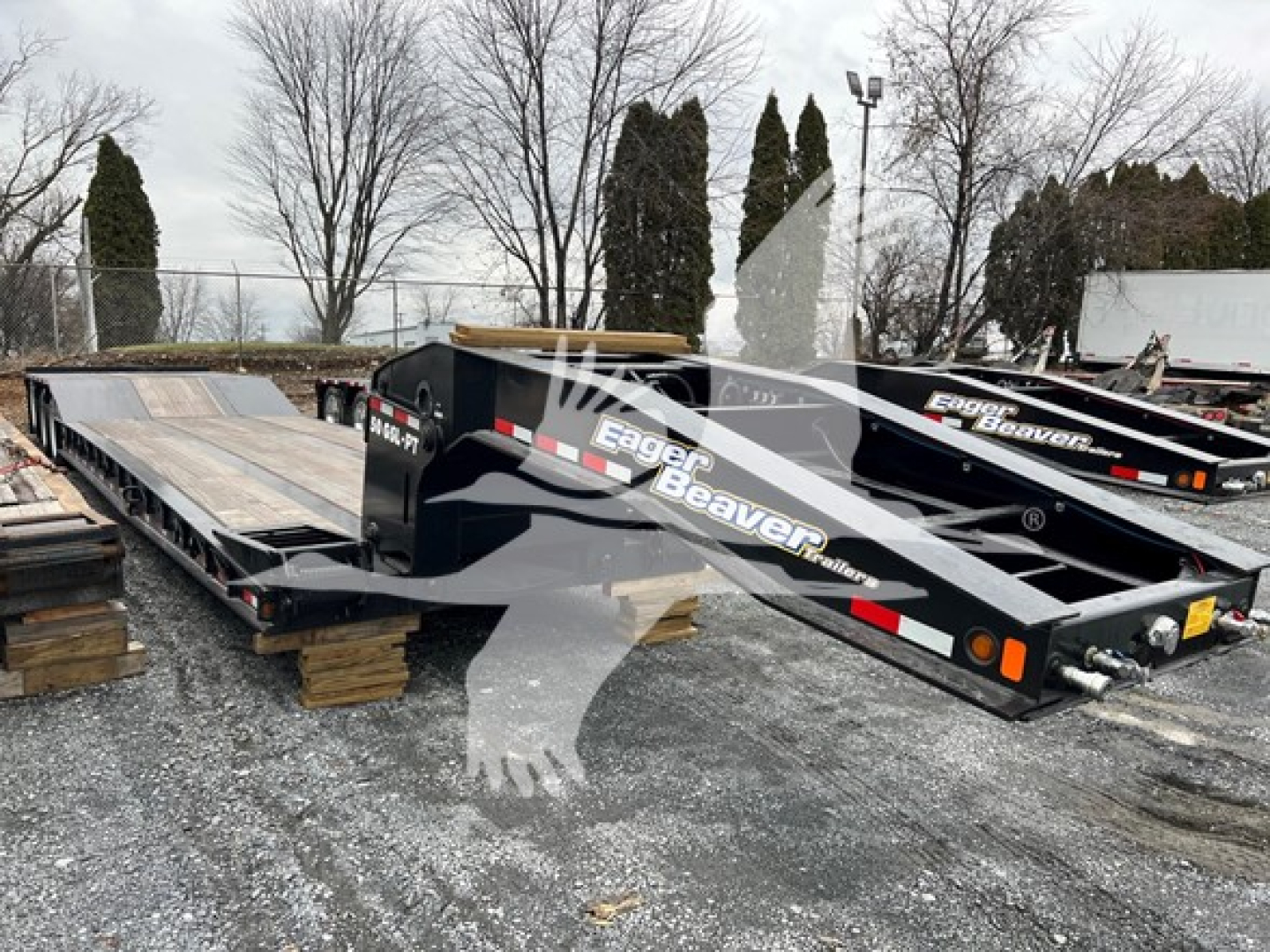 Trailing view of a black Eager Beaver 50 Ton Hydraulic Detachable Paver trailer with logo and white text, parked on wooden blocks in a yard.