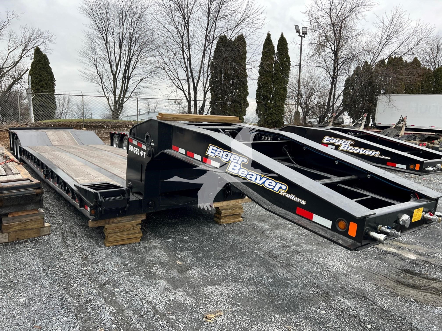 Lowboy trailer in a lot showing Eager Beaver branding and heavy-duty tilt-bed sections.