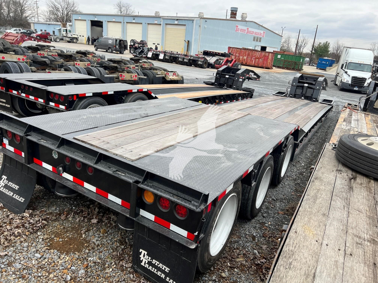 Paver trailer in a yard showing aluminum decking, triple-axle arrangement, rear underride lights, and reflective tape.