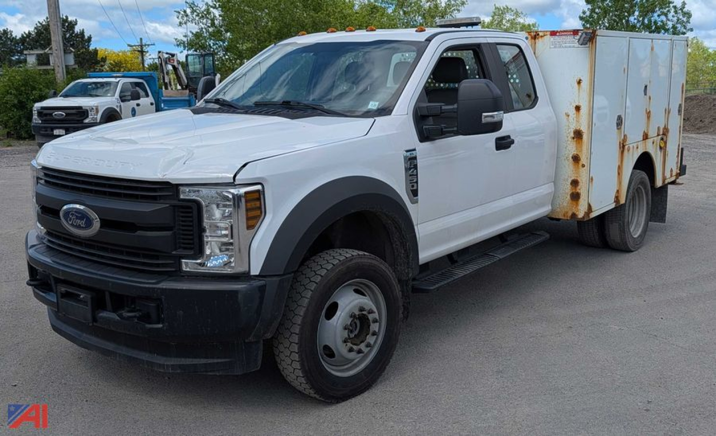Ford F-450 Super Duty service truck with white cab and rusted utility box on the bed, front grille and bumper visible, side mirrors, running boards, standard steel wheels.