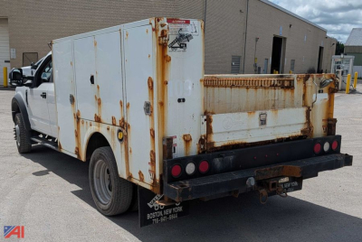 Service body utility truck rear and side view showing rusted white utility bed with storage compartments on a Ford F-450 Super Duty, dual rear wheels, service rear bumper, and warning labels.